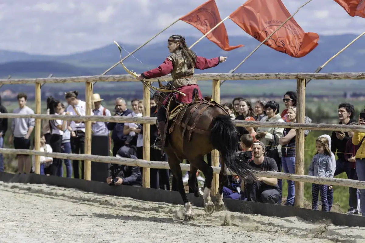 Un călăreț în costum vișiniu ține arcul întins în fața publicului.