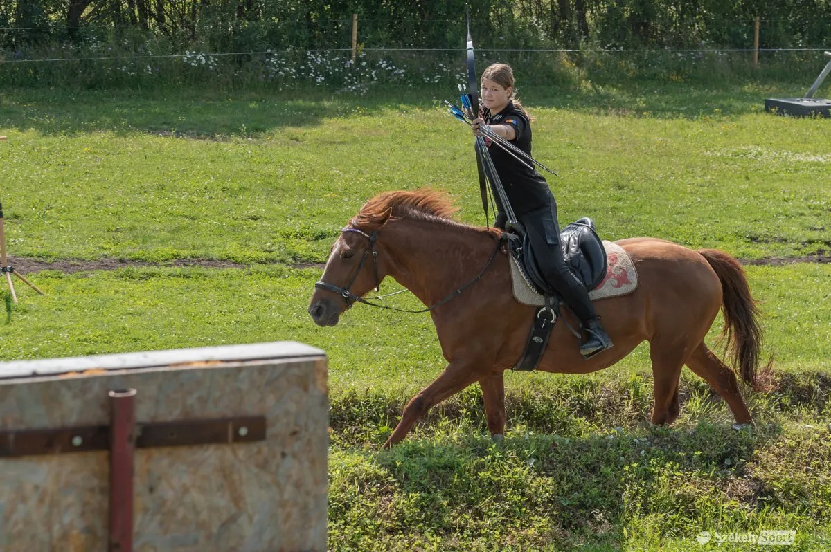 Un arcaș ecvestru întinde arcul în timp ce calul urcă o pantă.